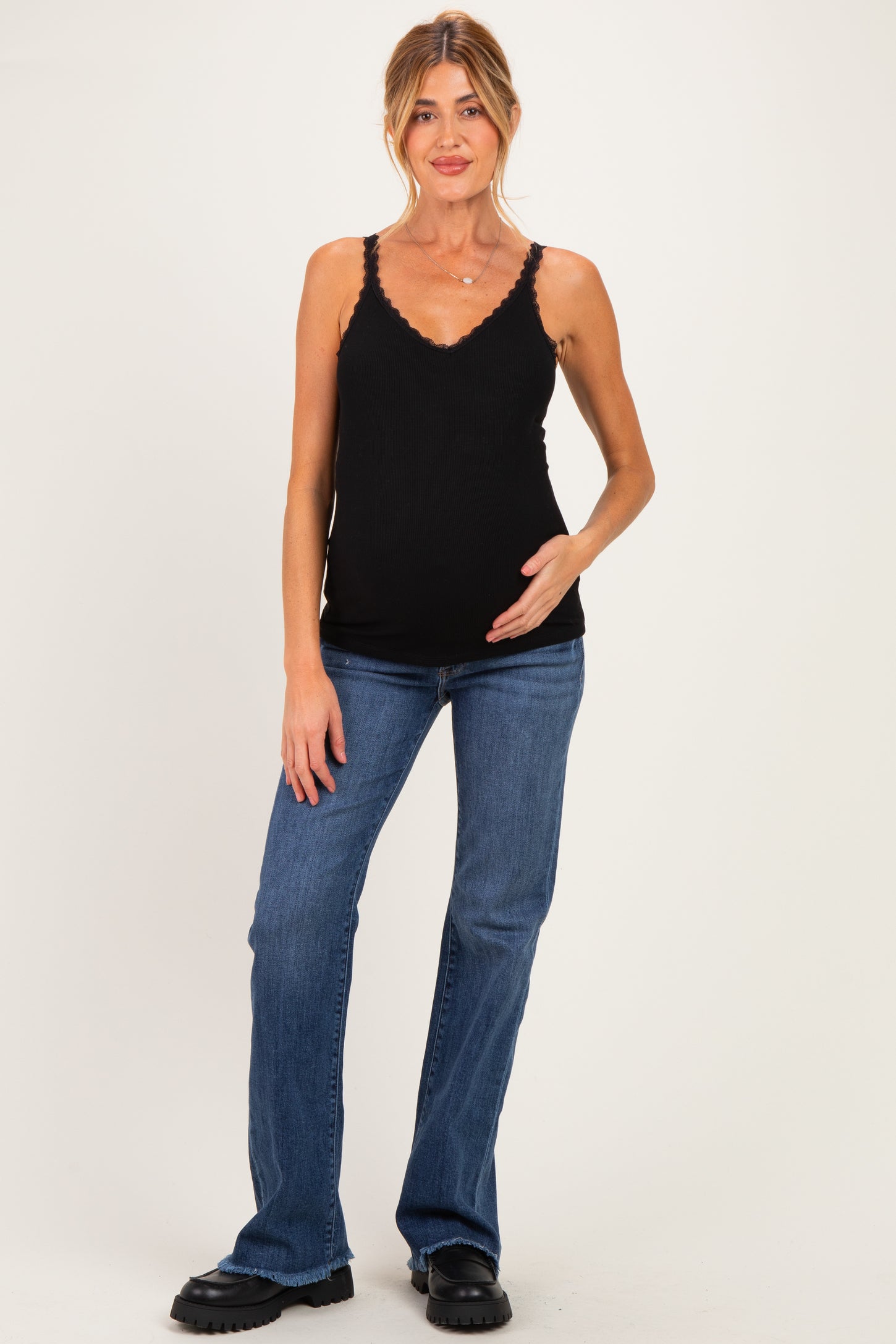 woman wearing a black maternity tank top and blue jeans, gently cradling her baby bump