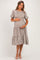 woman wearing a beige floral maternity dress with puff sleeves and tiered skirt, holding her baby bump