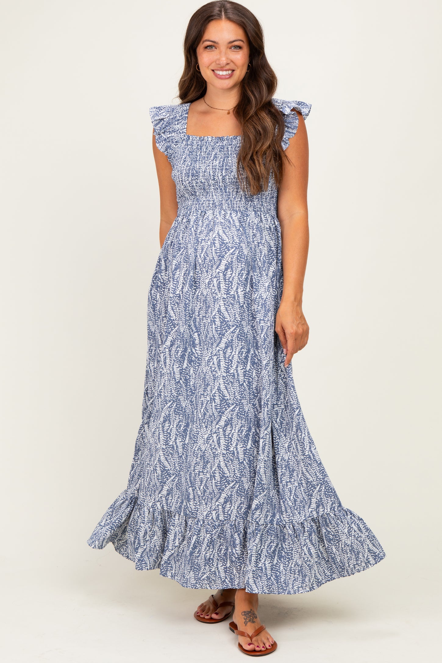 woman wearing a blue floral patterned maternity maxi dress with flutter sleeves and a smocked bodice