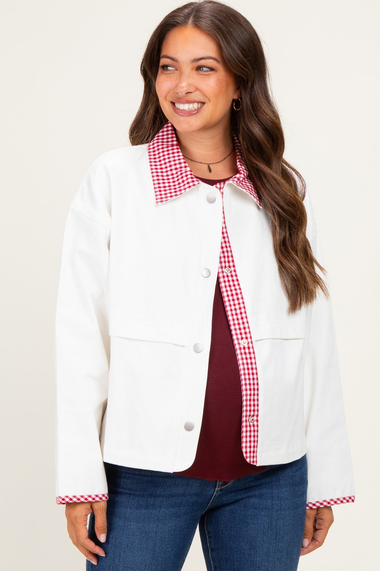 woman wearing a white cropped jacket with a red gingham collar and sleeves, styled with a maroon top and blue jeans
