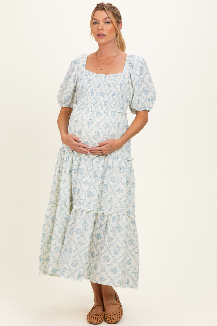 woman wearing a blue patterned maternity dress with puff sleeves and a tiered skirt, cradling her baby bump