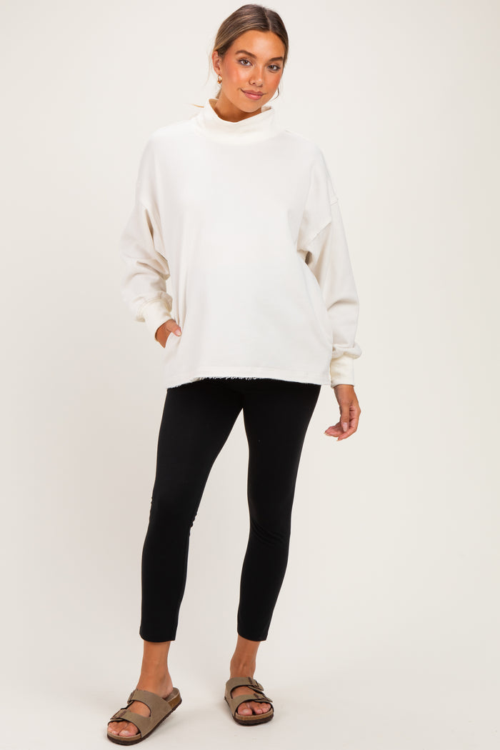 woman wearing a cream oversized maternity sweatshirt with a high neck and black maternity leggings