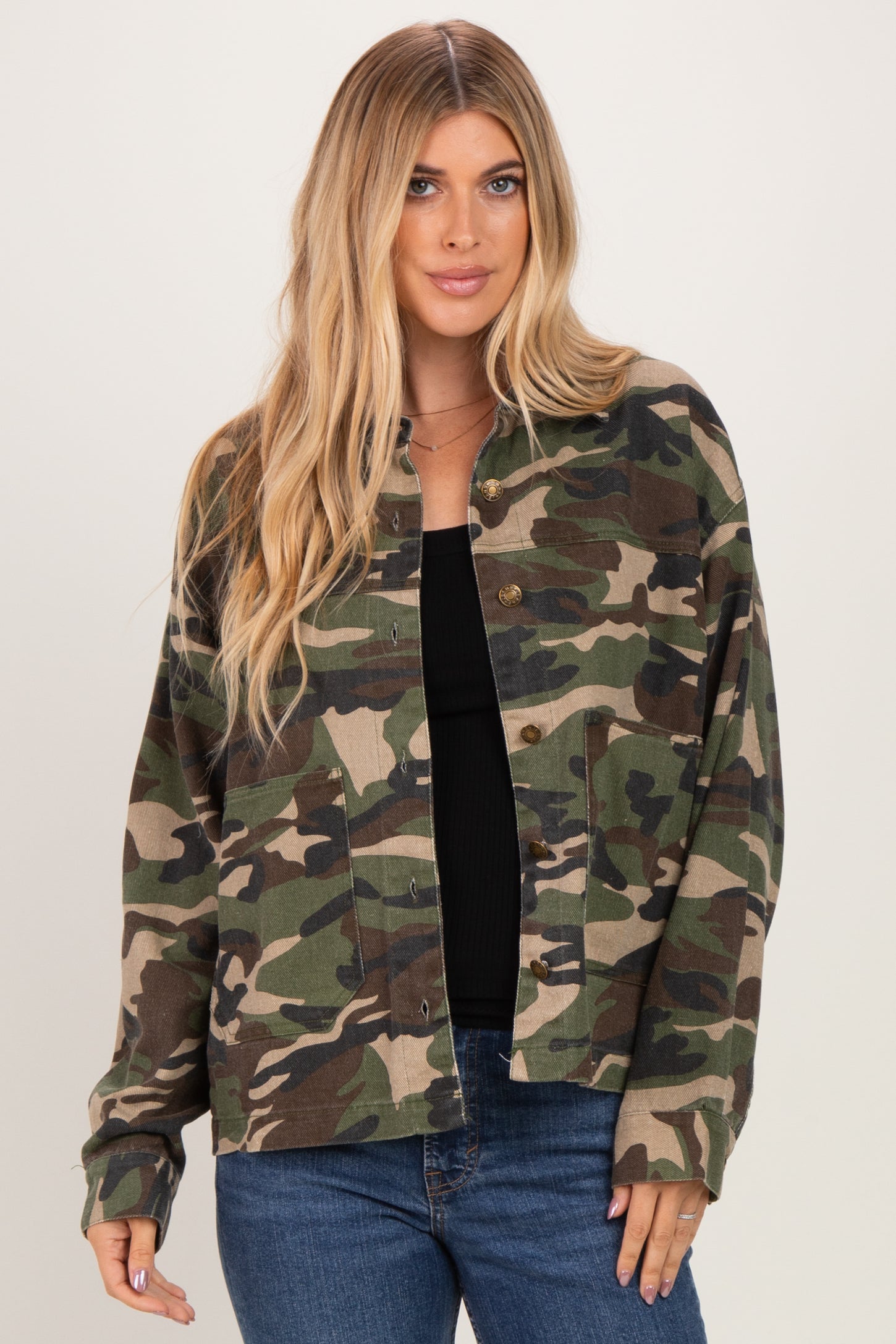 woman wearing a green camouflage button-up jacket over a black top, styled with blue jeans