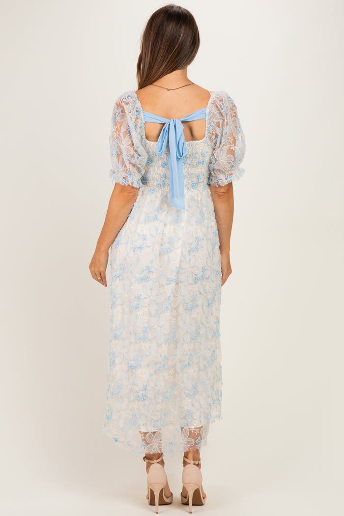 woman wearing a light blue lace maternity dress with short puff sleeves and a bow detail at the back