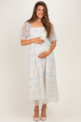 woman wearing a light blue floral lace maternity dress and showing her baby bump