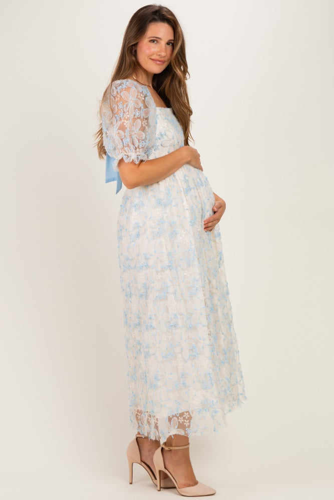 woman wearing a light blue lace maternity dress with a ribbon detail, holding her baby bump