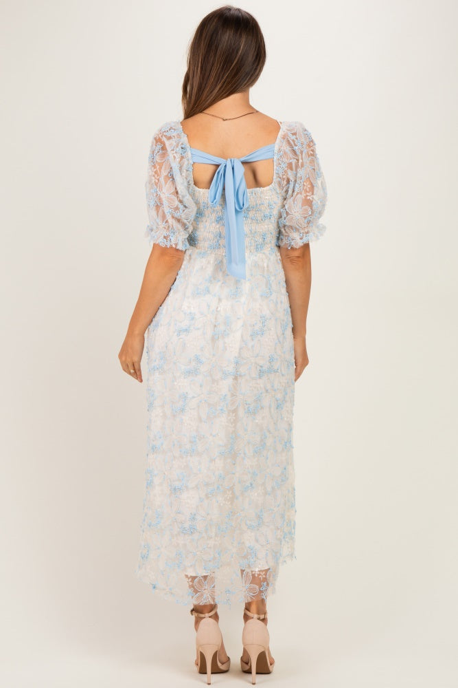 woman wearing a light blue lace maternity dress with short puff sleeves and a bow detail at the back