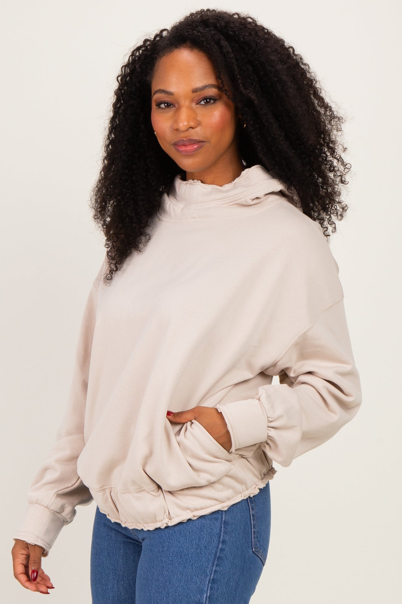woman wearing a beige oversized hoodie with a gathered hem and pockets, styled with denim jeans