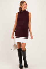 woman wearing a burgundy ribbed maternity dress with a white pleated skirt and holding a small handbag