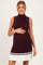 woman wearing a burgundy ribbed maternity dress with a sleeveless design and pleated white skirt, showing her baby bump