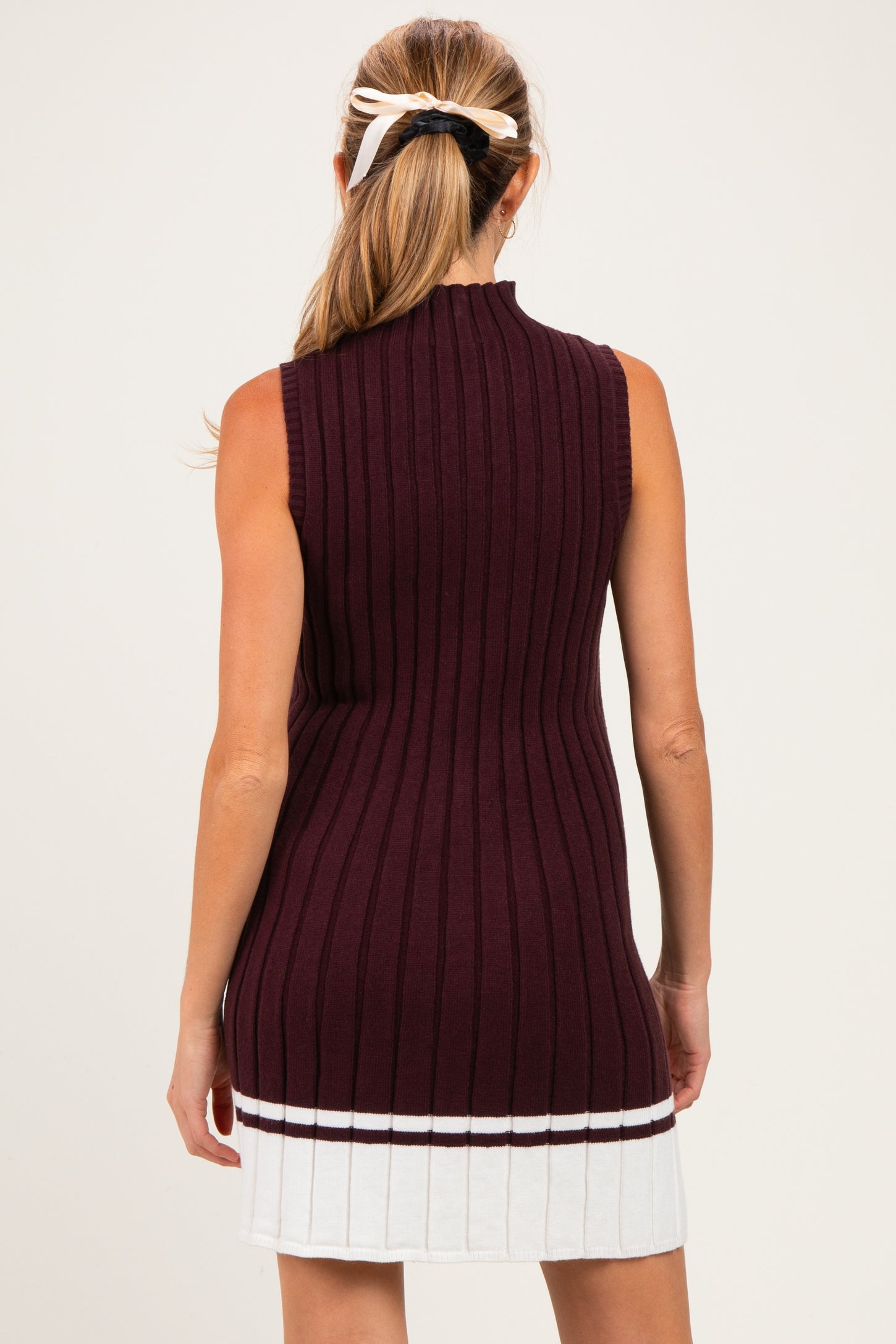 woman wearing a sleeveless burgundy knit maternity tunic dress with ribbed texture and white stripe at the hem