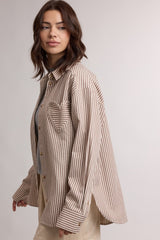 woman wearing a beige and white striped oversized button-up shirt styled casually with a gray top underneath