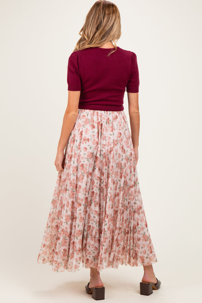 woman wearing a maroon short sleeve top and a flowy pink floral maternity skirt from the back