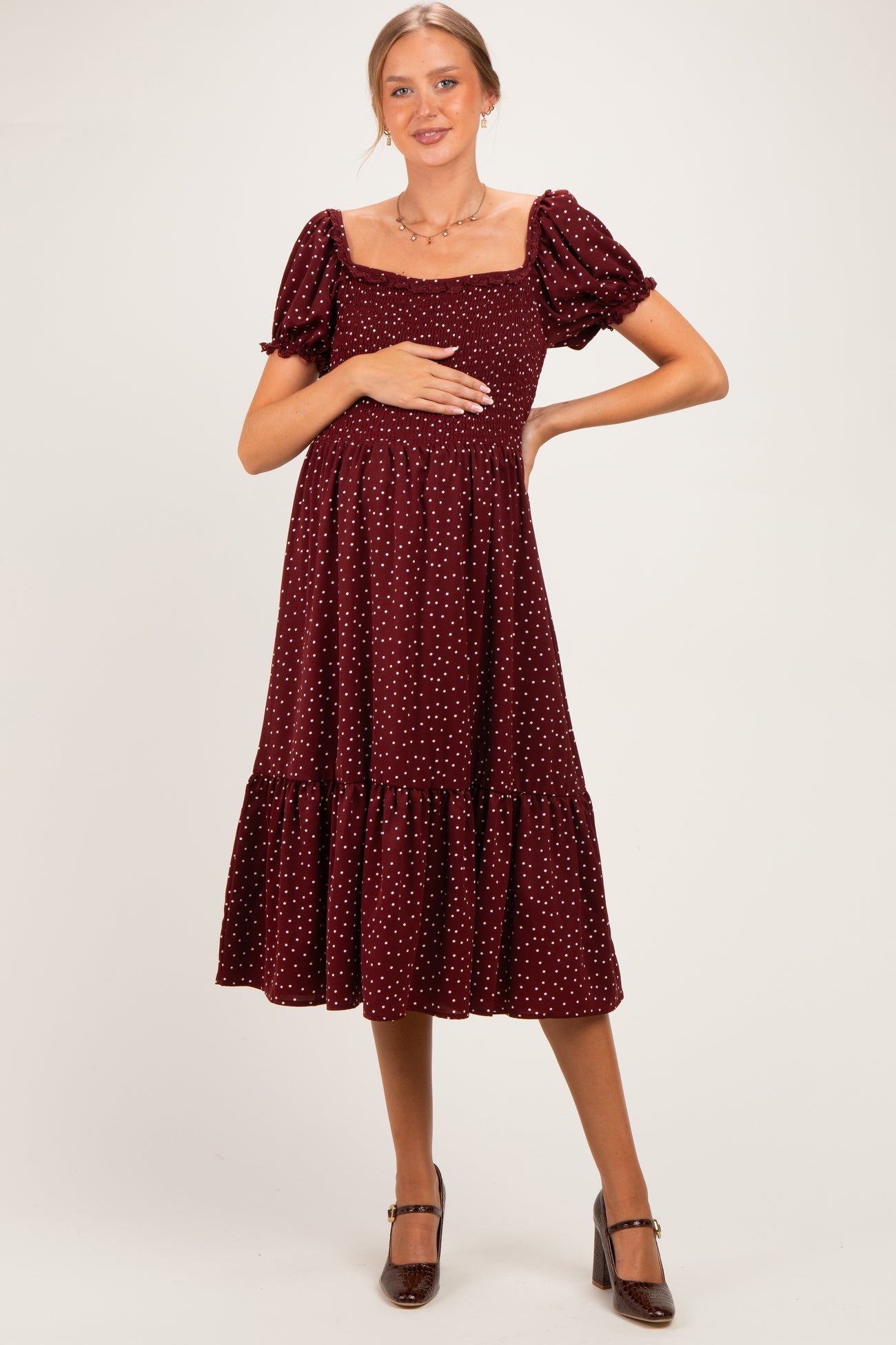 woman wearing a burgundy polka dot maternity dress with a square neckline and puff sleeves, holding her baby bump