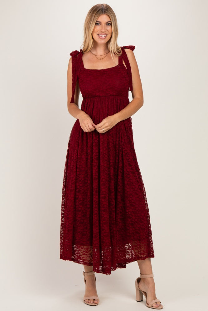 woman wearing a burgundy lace maxi dress with bow tie shoulder straps and a fitted bodice