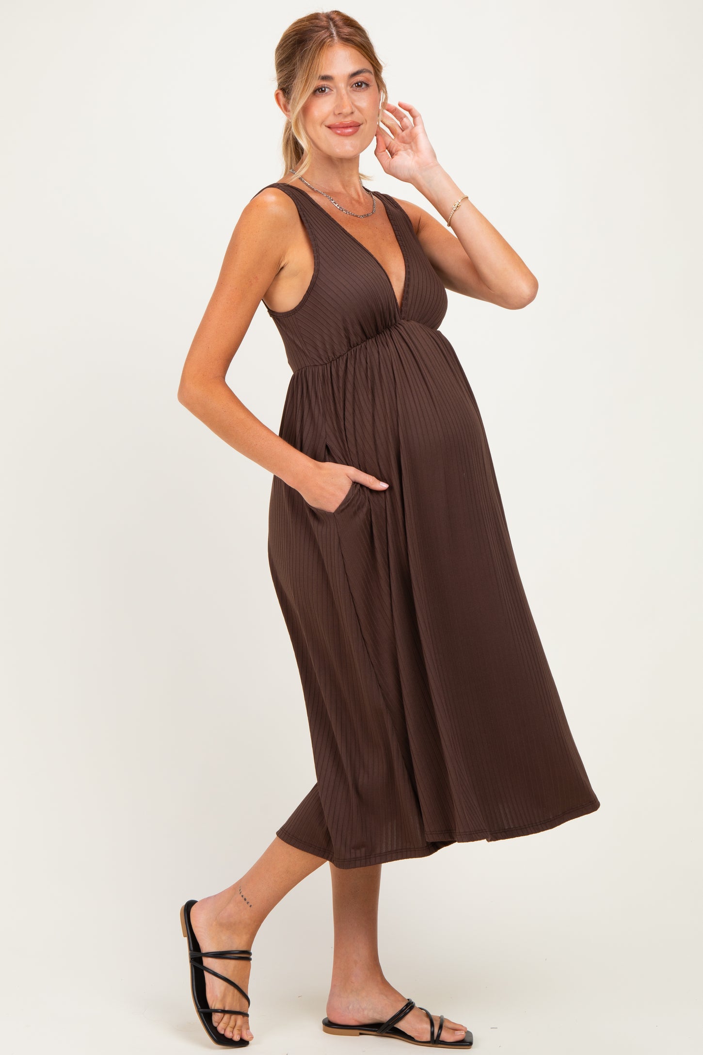 woman wearing a dark brown pleated maternity dress with pockets and showing her baby bump