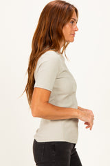 woman wearing a light gray ribbed short sleeve top and black jeans, standing in profile view