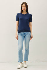 woman wearing a navy short sleeve knit top and light wash cropped jeans with white sneakers