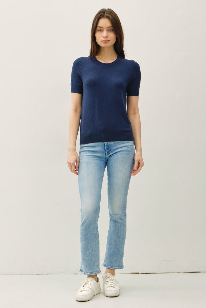 woman wearing a navy short sleeve knit top and light wash cropped jeans with white sneakers