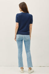 woman wearing a navy short sleeve top with light blue flared jeans and sneakers, viewed from the back