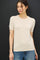 woman wearing a short sleeve beige knit top paired with light blue jeans against a dark background