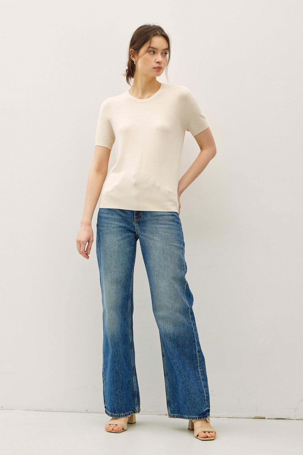 woman wearing a cream short sleeve sweater paired with light blue flared jeans and beige sandals
