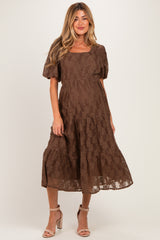 woman wearing a brown lace maternity dress with short puff sleeves and a flowing skirt, highlighting her baby bump