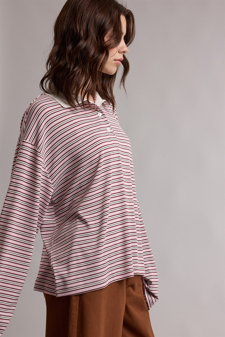 woman wearing a pink and white striped oversized polo shirt with long sleeves and a casual fit