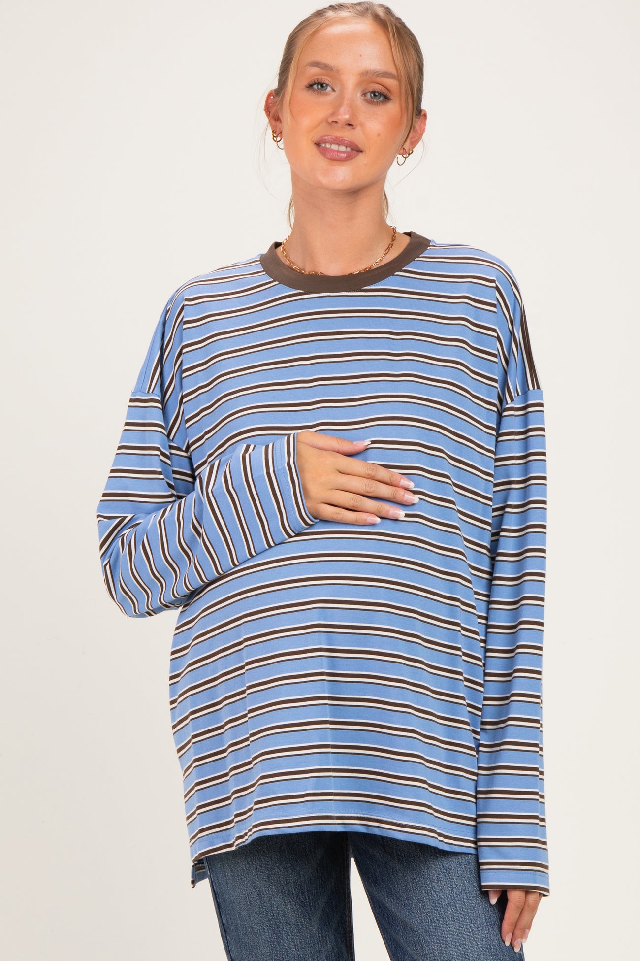 woman wearing a blue and brown striped long sleeve maternity top and holding her baby bump