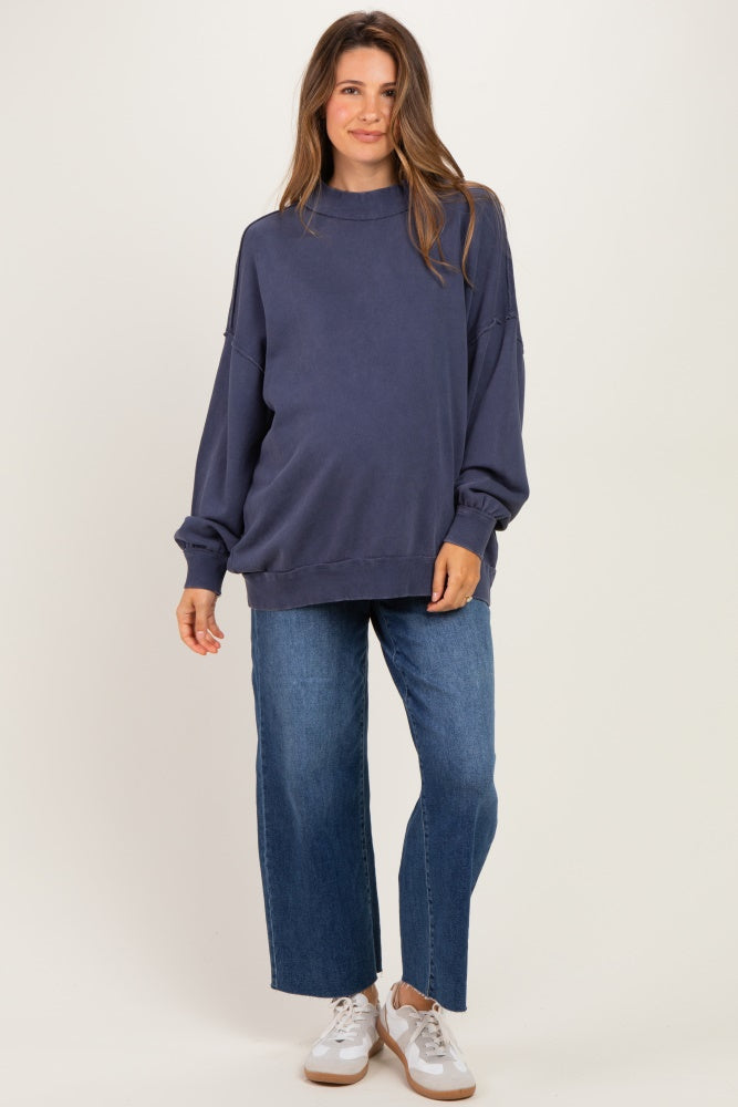 woman wearing a dark blue oversized maternity sweatshirt with baggy jeans and white sneakers, showing a baby bump