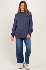 woman wearing a dark blue oversized maternity sweatshirt with baggy jeans and white sneakers, showing a baby bump