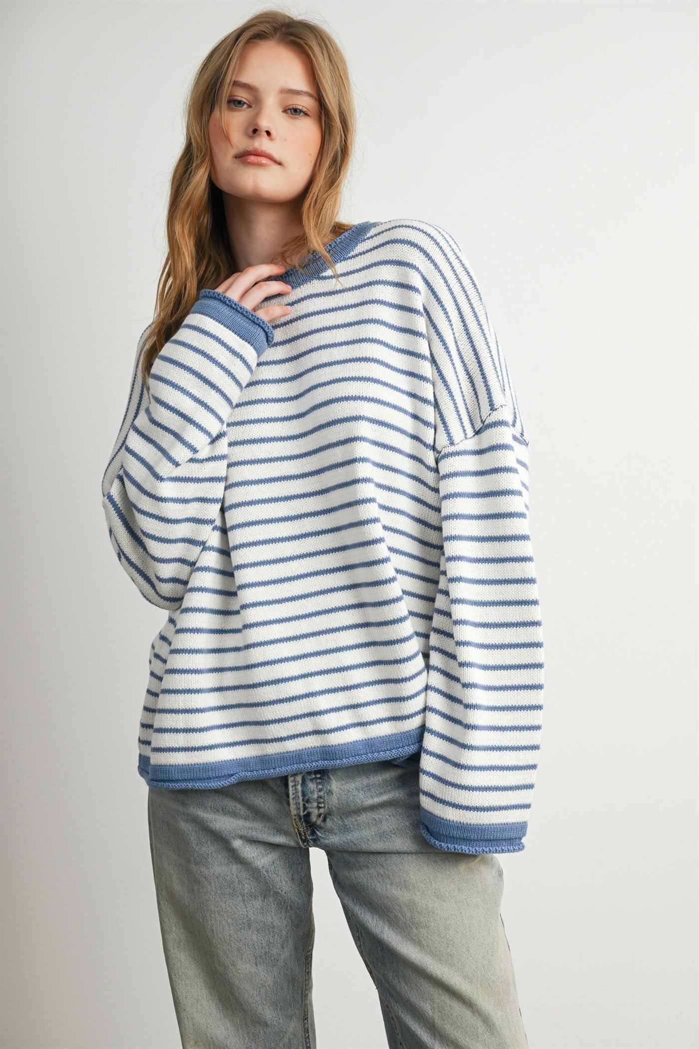 woman wearing a white and blue striped oversized sweater with a crew neck and dropped shoulders, paired with light blue jeans