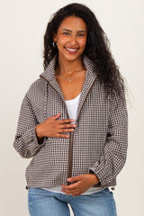 woman wearing a brown and white gingham patterned maternity jacket, gently holding her baby bump