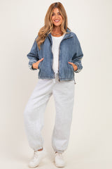 woman wearing a denim zip-up jacket over a white top and gray sweatpants, styled for maternity wear