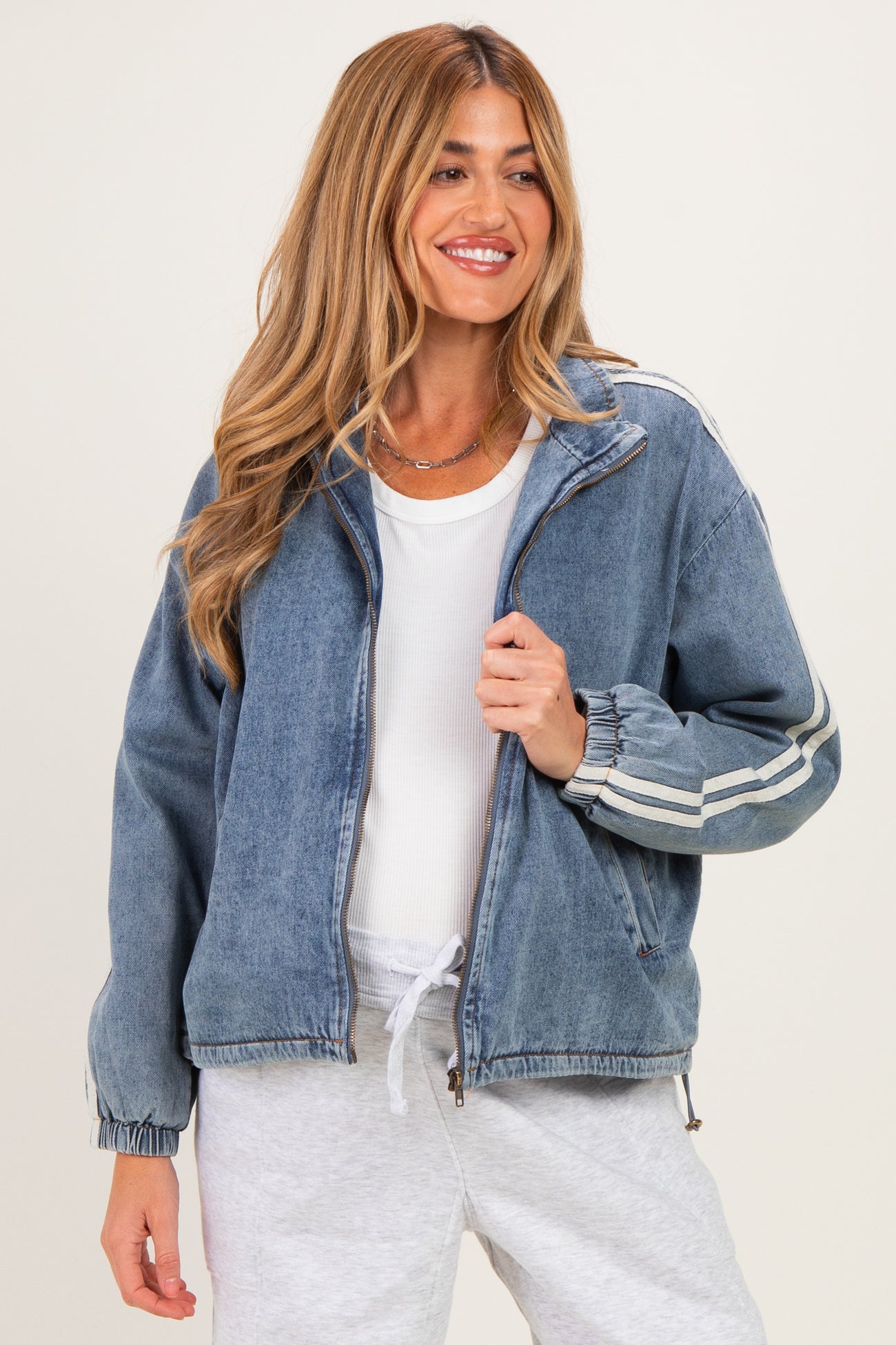 woman wearing a blue denim maternity jacket with white stripes and a white top, smiling and holding the jacket open
