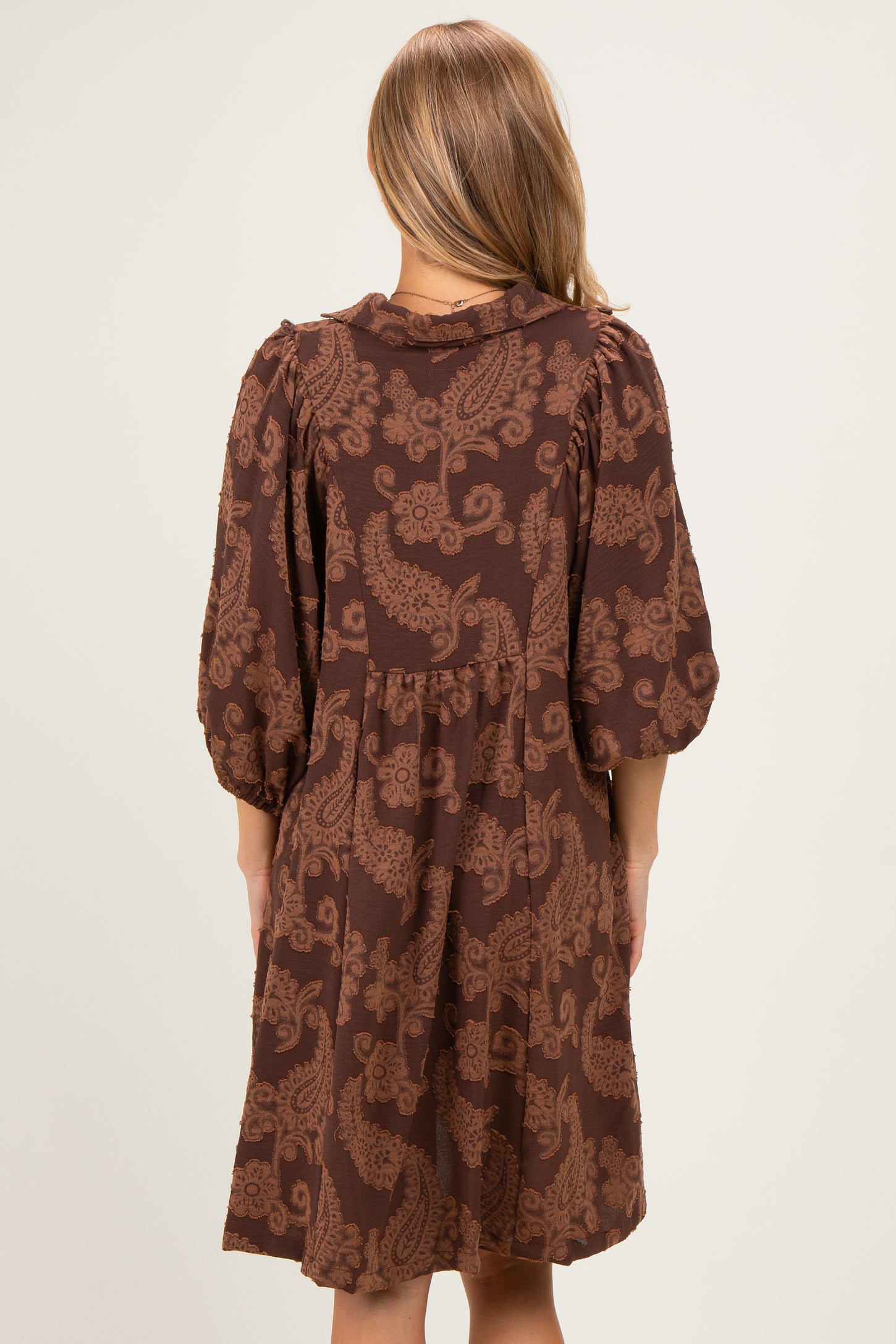 woman wearing a brown paisley print dress with puff sleeves and a relaxed fit from the back