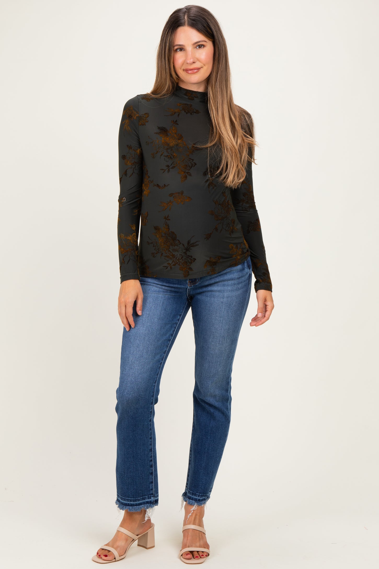 woman wearing a black floral maternity top with a high neck and long sleeves, paired with blue jeans