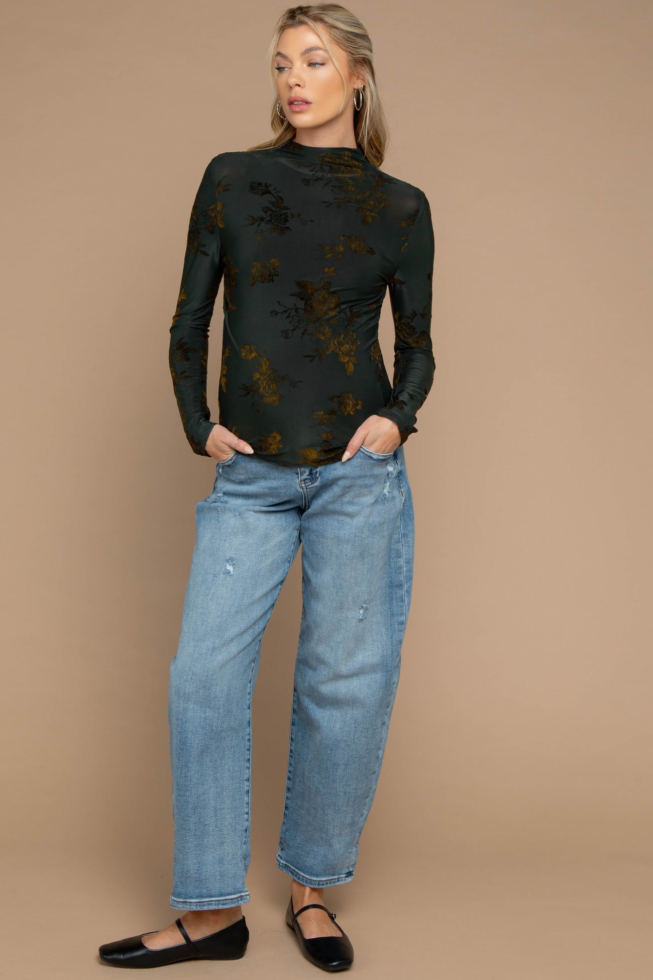 woman wearing a dark green floral long sleeve maternity top and distressed light blue jeans