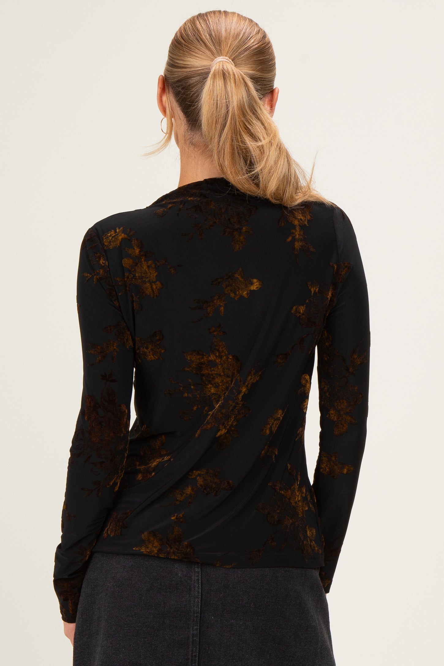 woman wearing a black long sleeve top with a floral print in shades of brown and gold, seen from the back