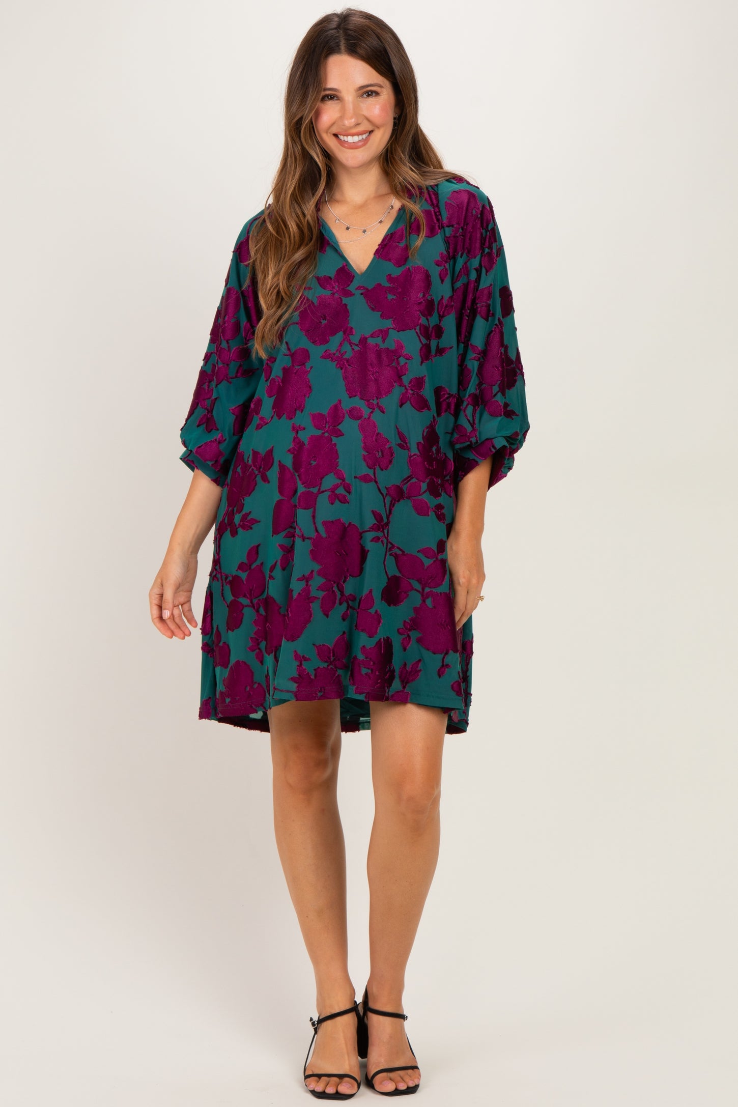 woman wearing a teal maternity dress with large purple floral print and a v-neckline