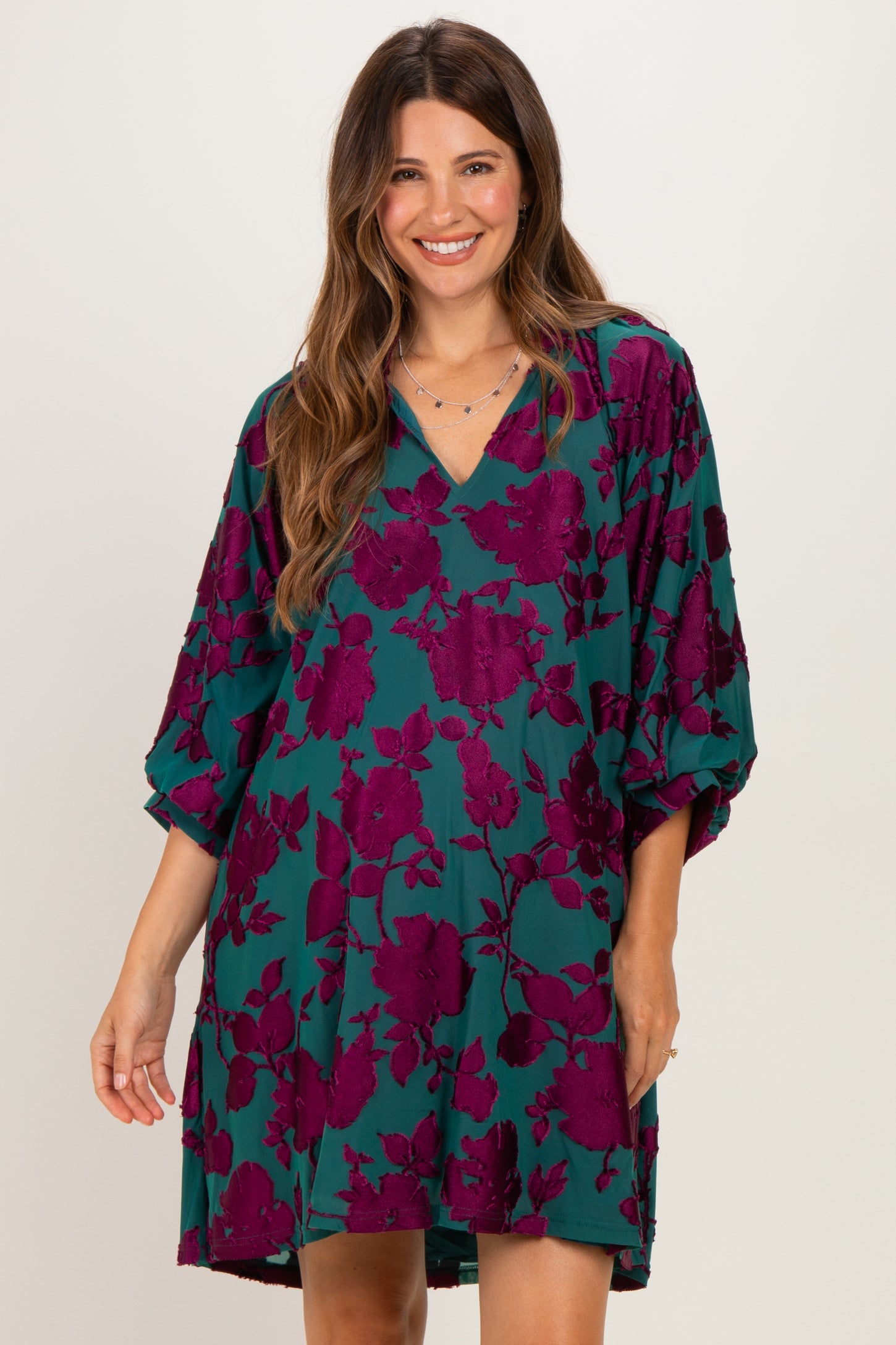 woman wearing a teal maternity dress with purple floral print and a v-neck, smiling at the camera