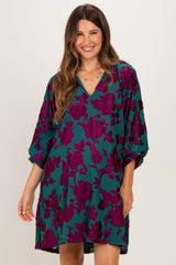 woman wearing a teal maternity dress with purple floral print and a v-neck, smiling at the camera