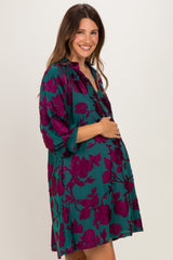 woman wearing a teal maternity dress with purple floral patterns and holding her baby bump