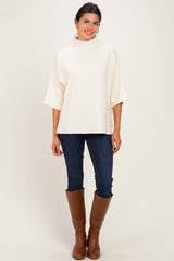 woman wearing a cream oversized top with wide sleeves and dark blue skinny jeans, paired with brown knee-high boots