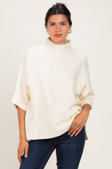 woman wearing a cream oversized pullover with a high neckline and rolled sleeves paired with blue jeans