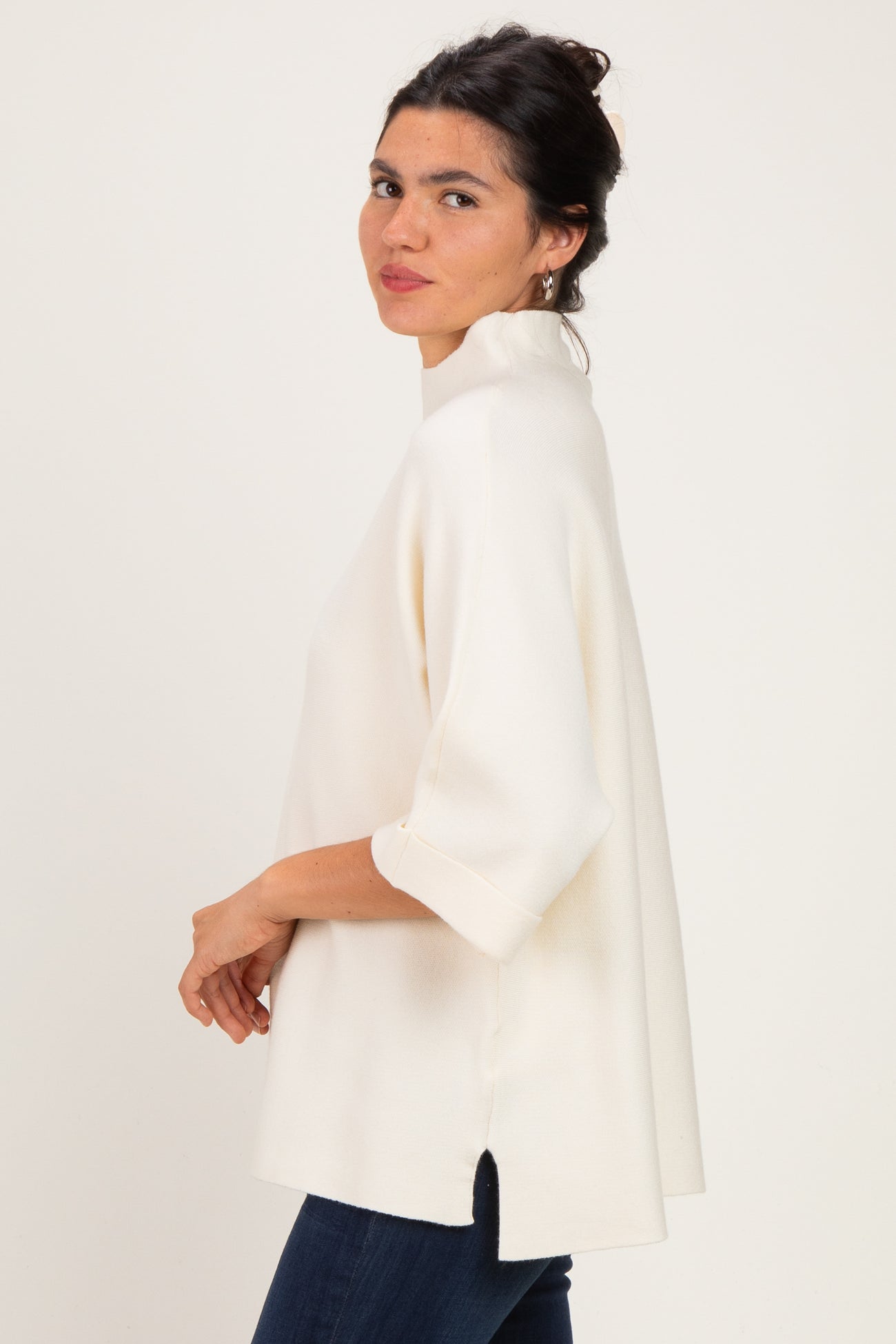 woman wearing a cream oversized top with three-quarter sleeves and side slits, paired with dark jeans