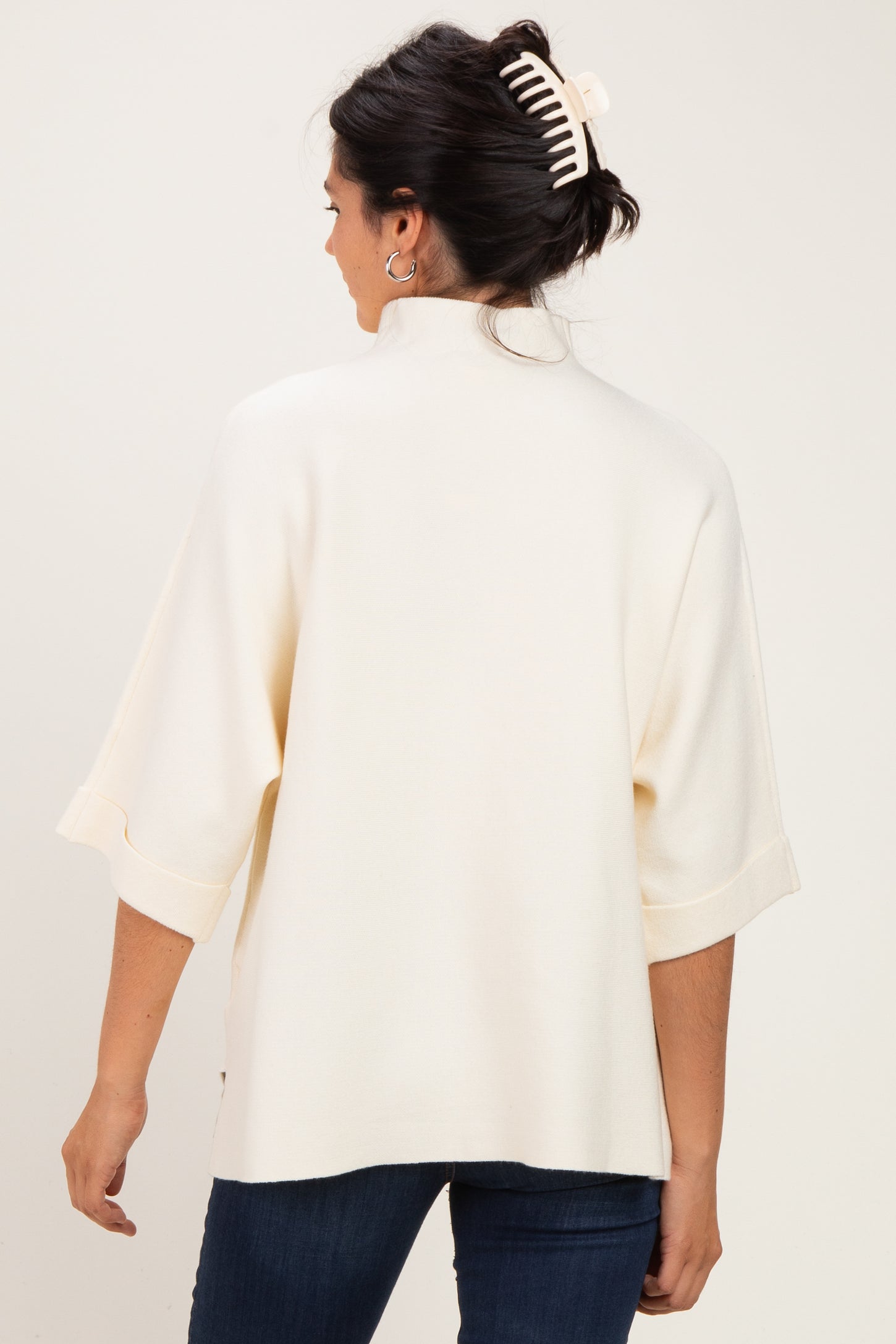 woman wearing a cream-colored oversized sweater with a high neck and wide sleeves, viewed from the back