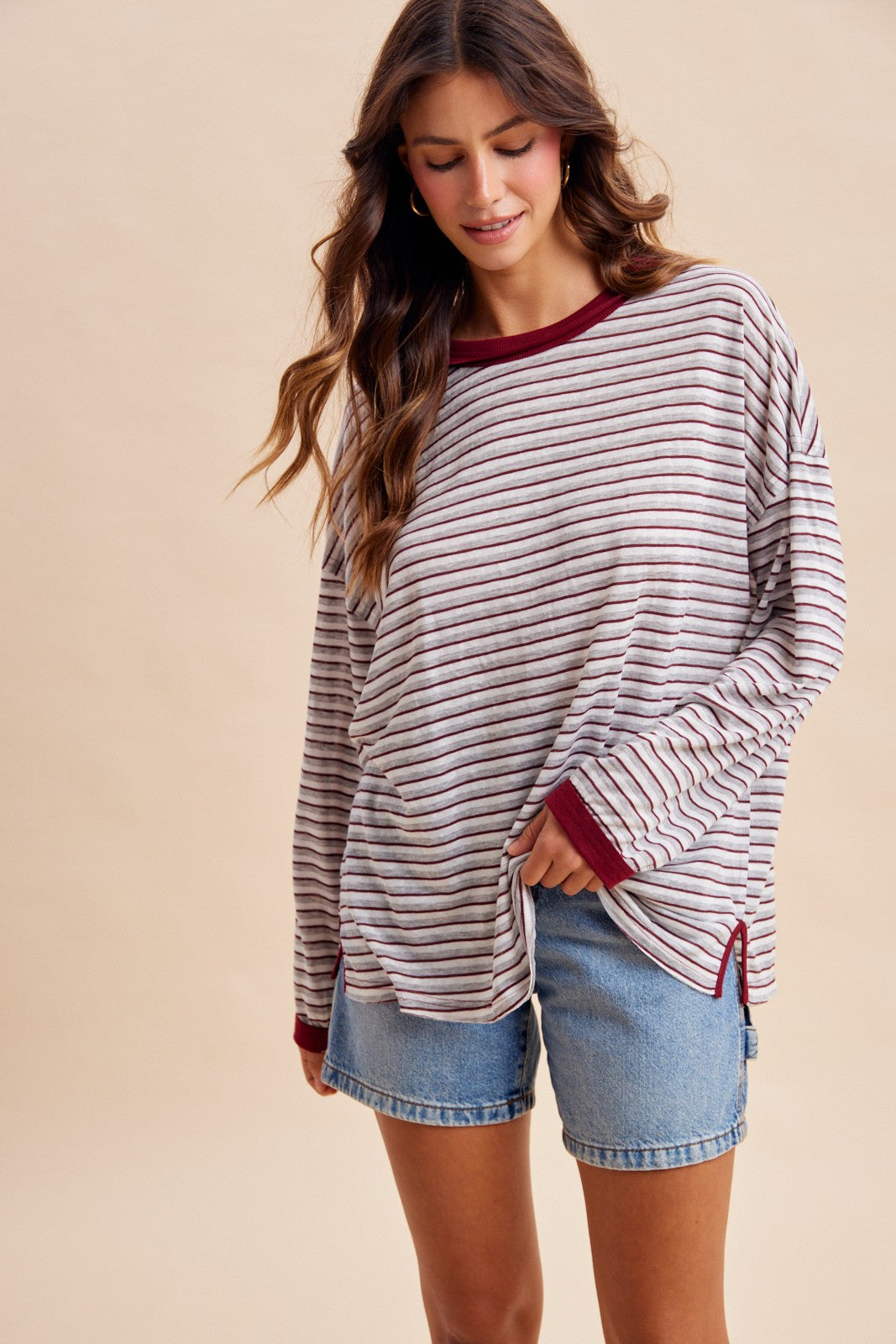 woman wearing a striped long sleeve top in shades of cream and burgundy paired with denim shorts
