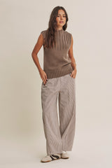 woman wearing a brown sleeveless textured sweater and striped wide-leg pants, standing with hands in pockets