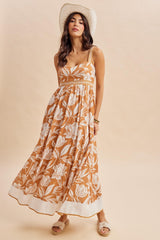 woman wearing a brown floral maxi dress with a square neckline and spaghetti straps, accessorized with a wide-brim hat
